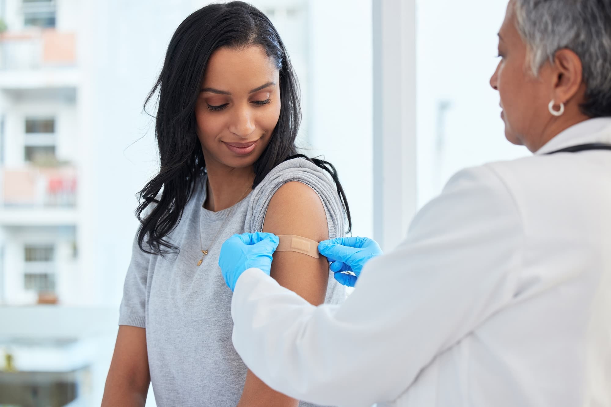 A female doctor applying a bandage to a woman patient after administering a vaccine