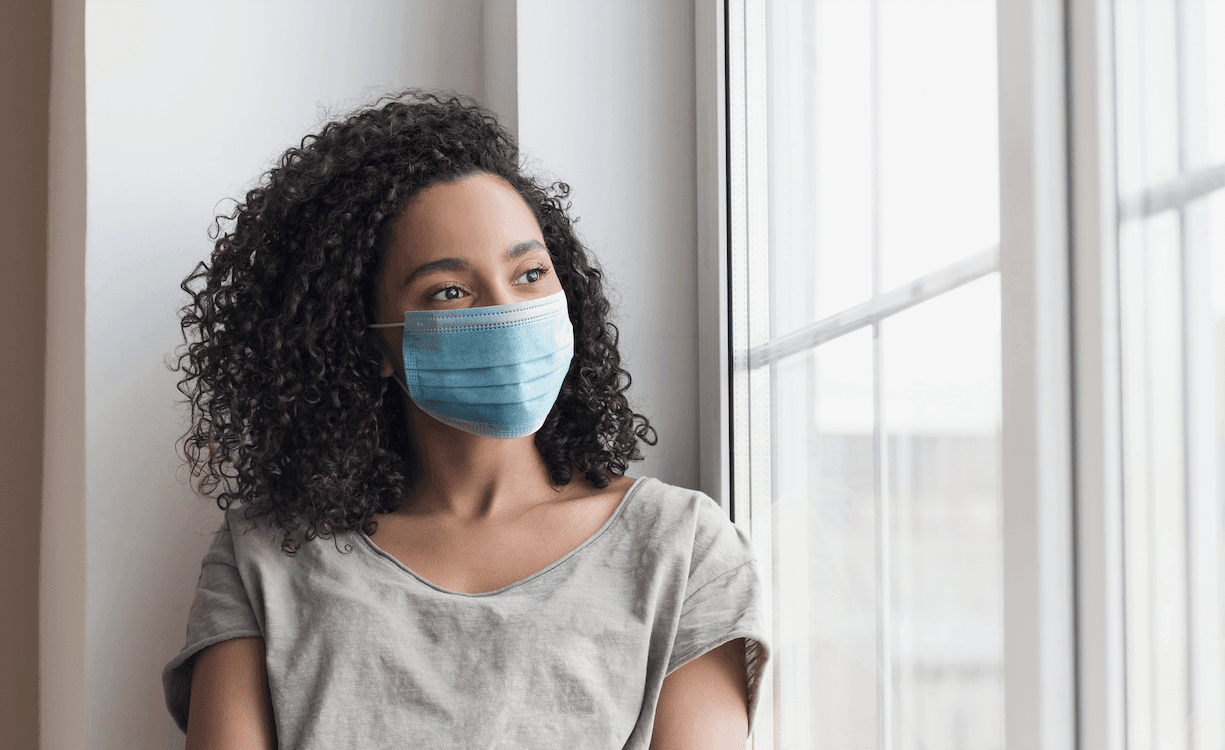 woman wearing a mask looking out a window