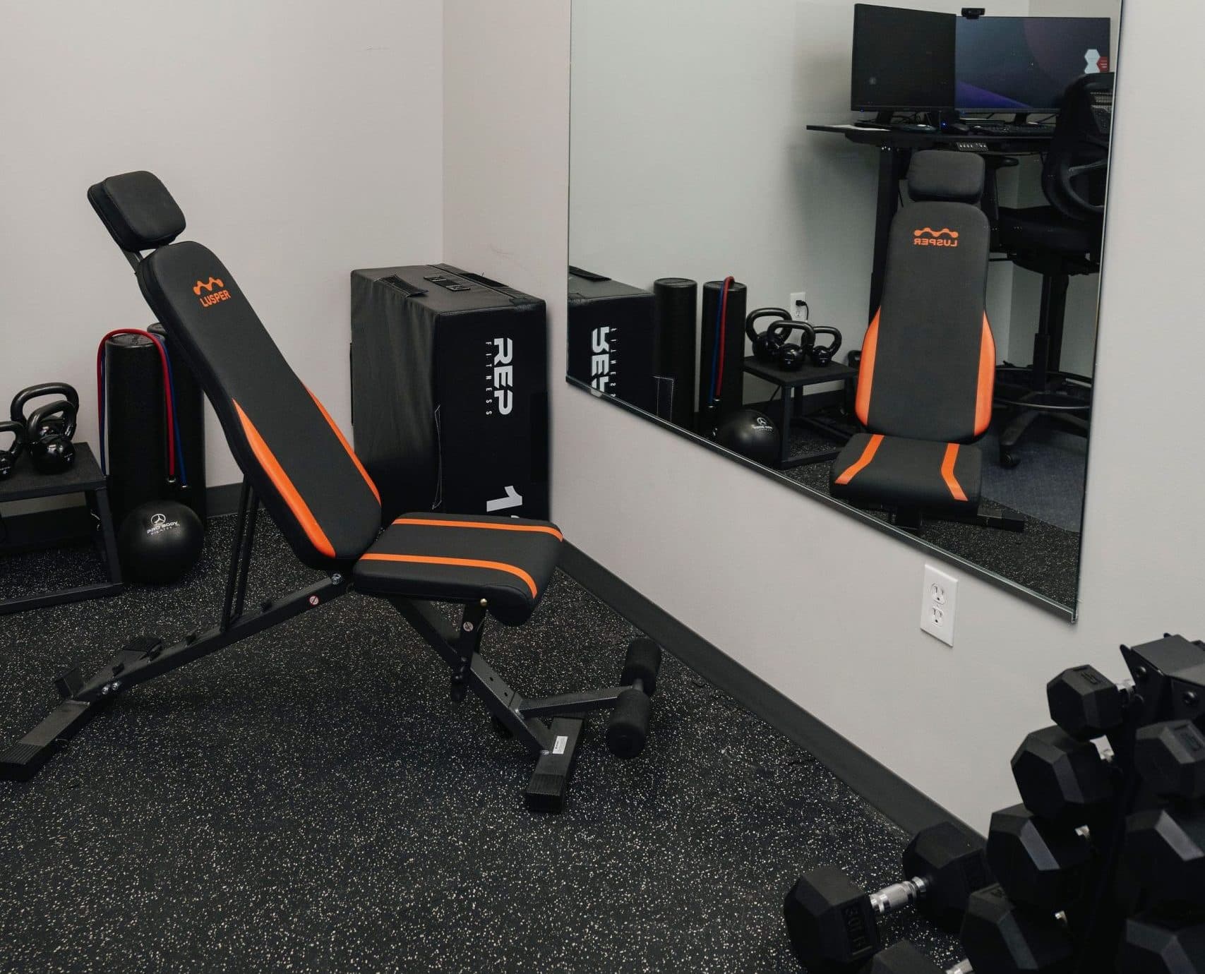 Image of Compact gym room with weight bench, dumbbells, kettlebells, and mirror.