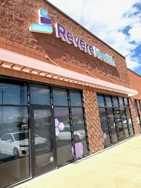 Image of Side angle of Revere Health building entrance, showing signage, reflection in glass, and purple window decals indicating the Weight Loss & Nutrition Center.