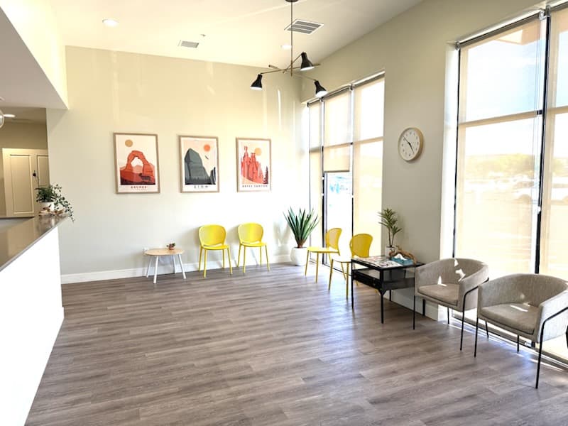 Image of Waiting room with yellow and gray chairs under portrait artwork, providing a cheerful, comfortable space for patients.