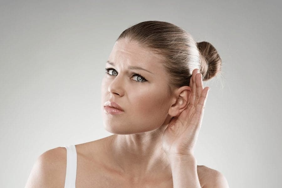 woman cupping ear to hear better