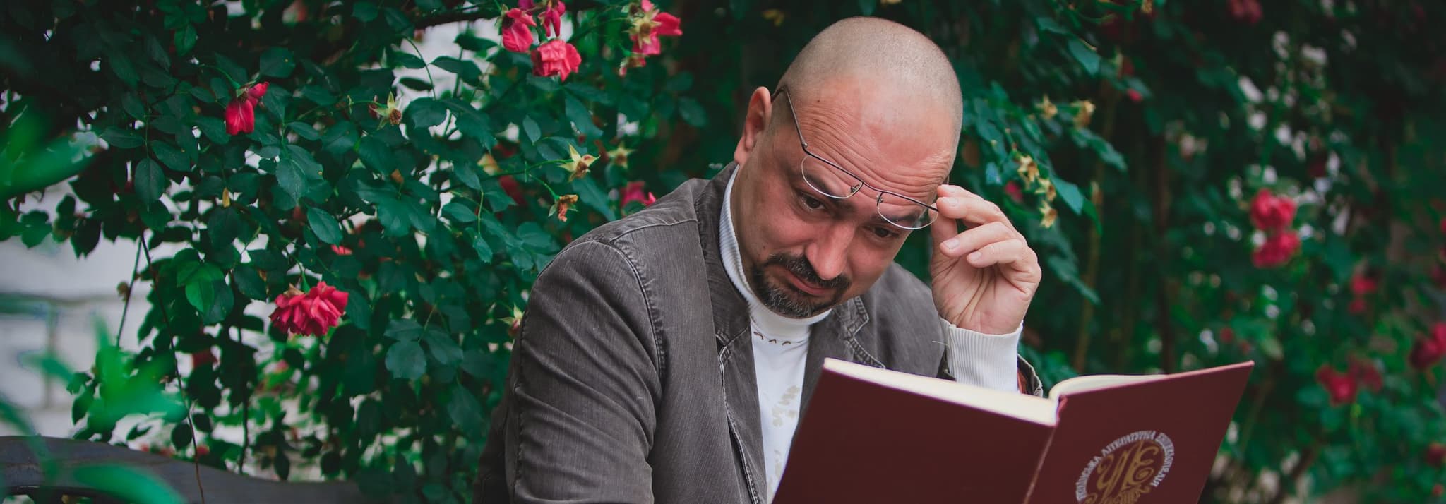 Picture of man trying to read outside on park bench, lifting up glasses to see