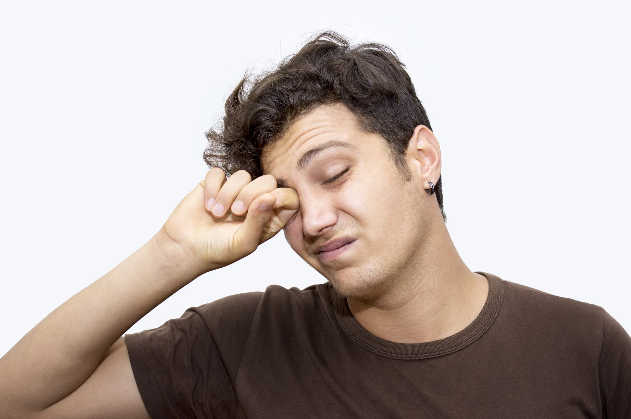 Picture of Portrait of napping young man rubbing his eyes isolated on white. Horizontal composition. Studio shot. Image developed from RAW format. Tired teenage boy has got short, curly, brown hair.