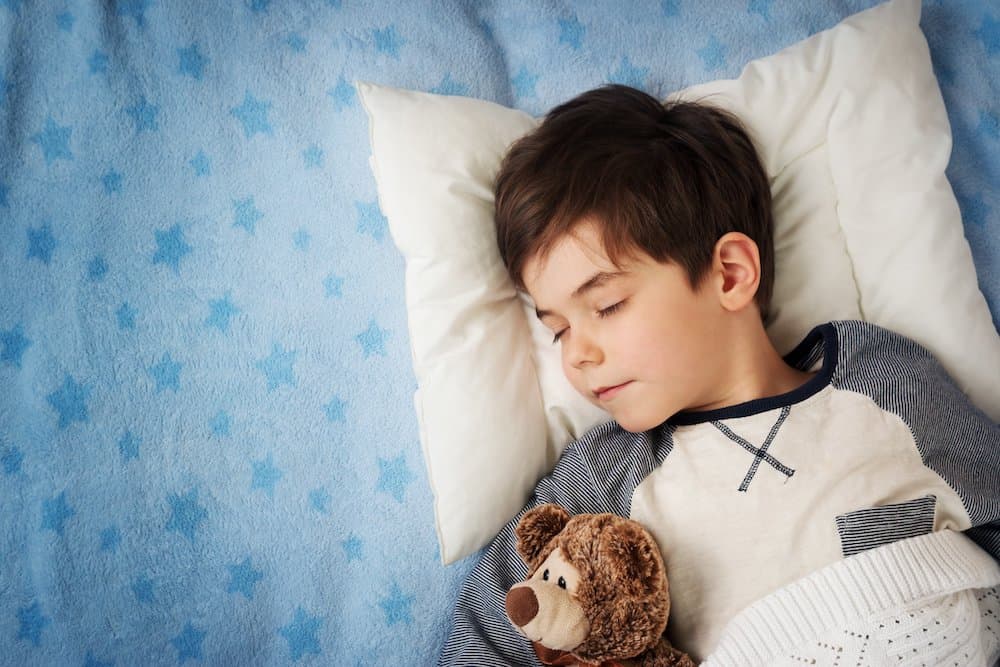 Picture of six years old child sleeping in bed with stuffed bear