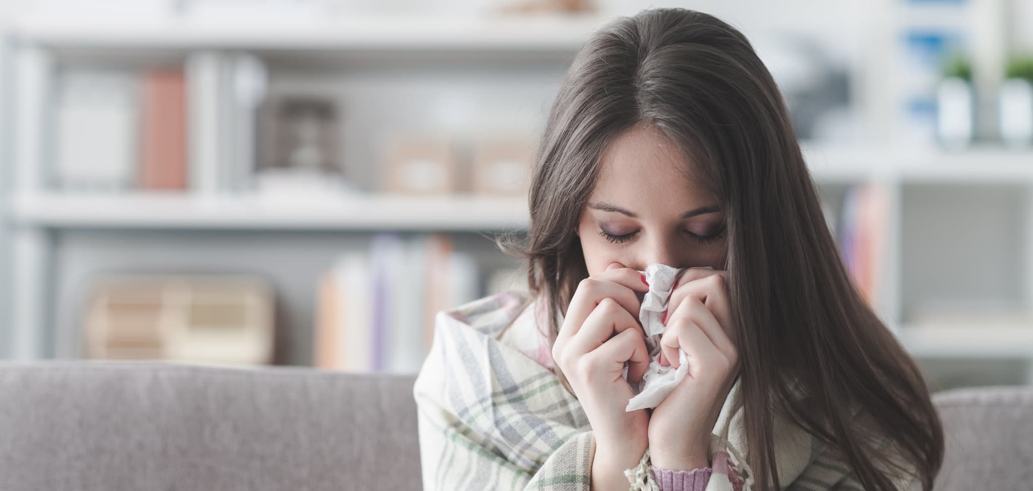 Picture of Sick young woman at home on the sofa with a cold, she is covering with a blanket and blowing her nose