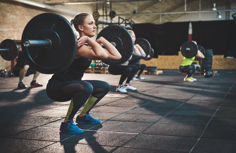 Picture of Fit young woman lifting barbells looking focused, working out in a gym with other people