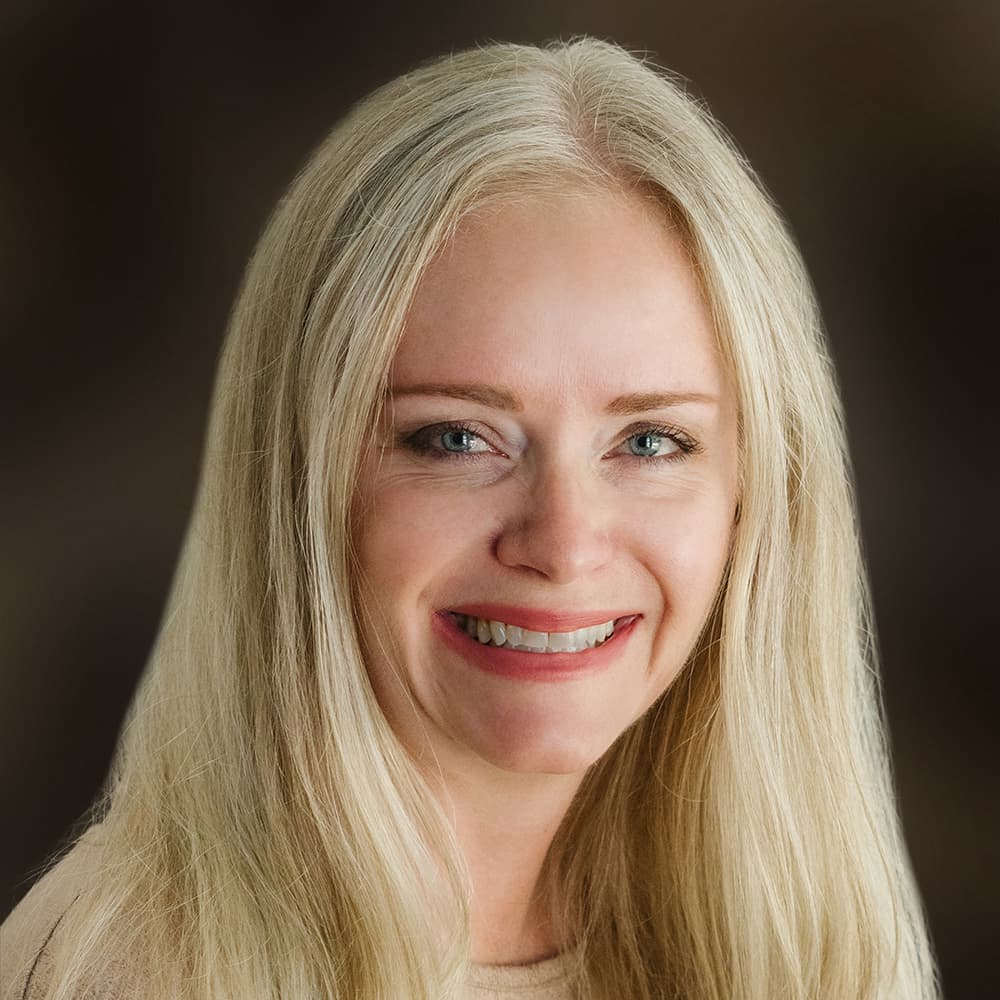 Image of Portrait of Heather Harrison, DO. A woman with long light blonde hair and smiling against a brown background.