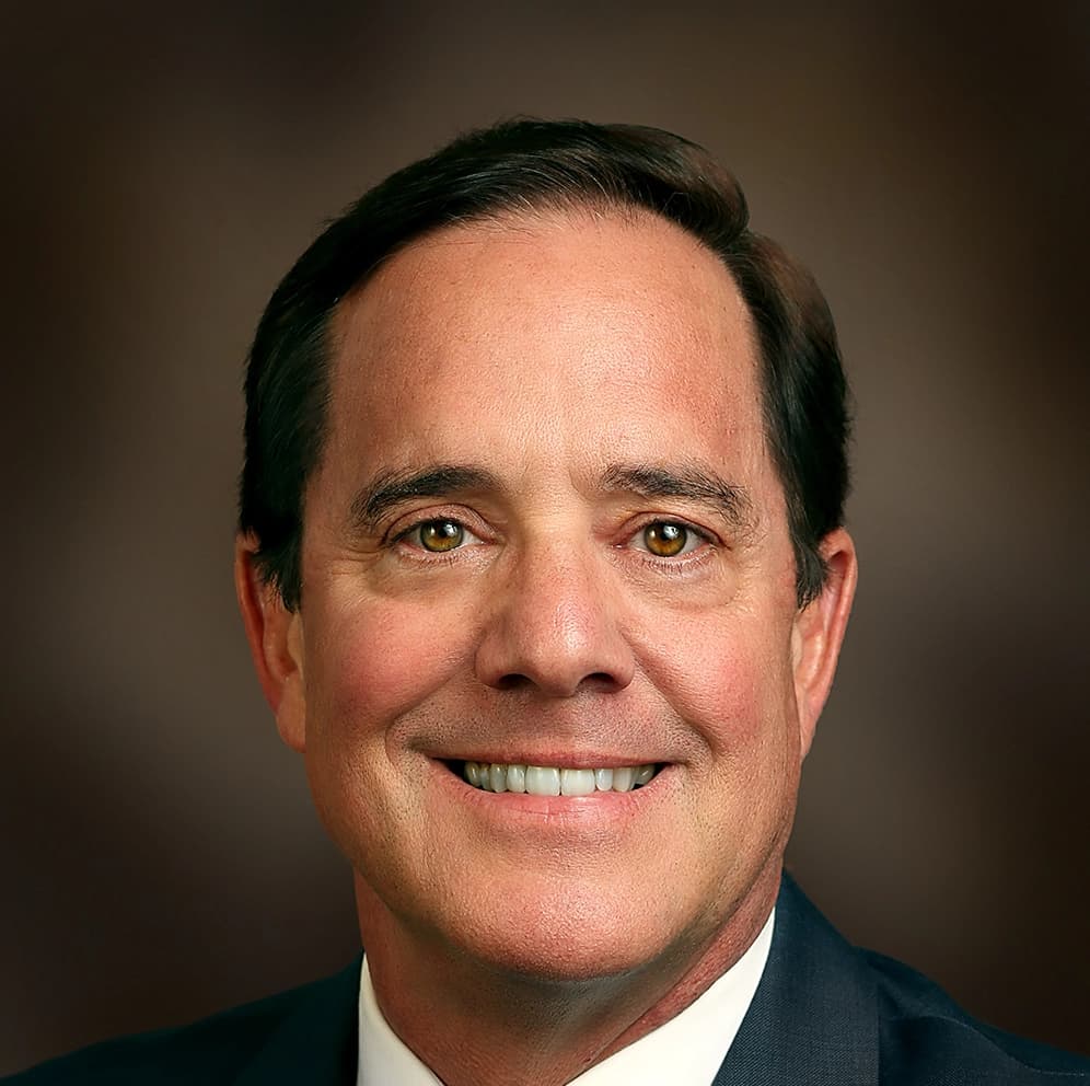 Image of Portrait of Bob Freeze, a man with short dark hair, wearing a suit and smiling against a brown background