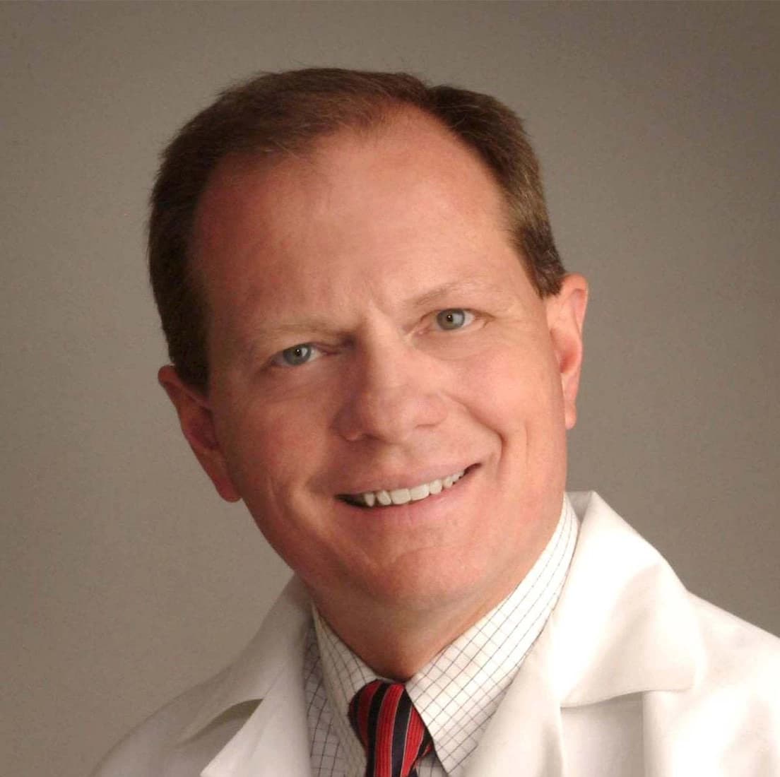 Portrait of Curtis Johnson, MD, a man with short brown hair, wearing a white coat and smiling against a light brown background.