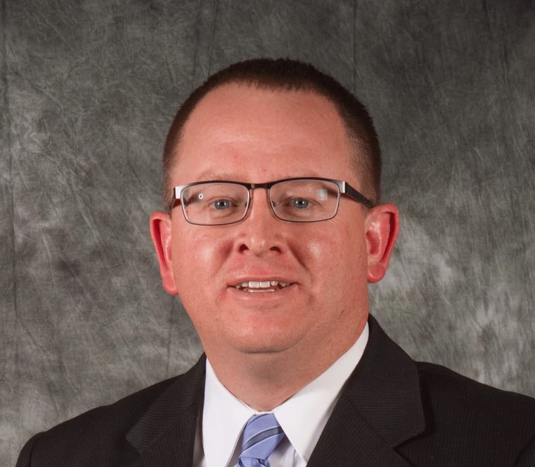 Portrait of Curtis Carter, MD, a man with short brown hair, wearing a suit and smiling against a gray background.