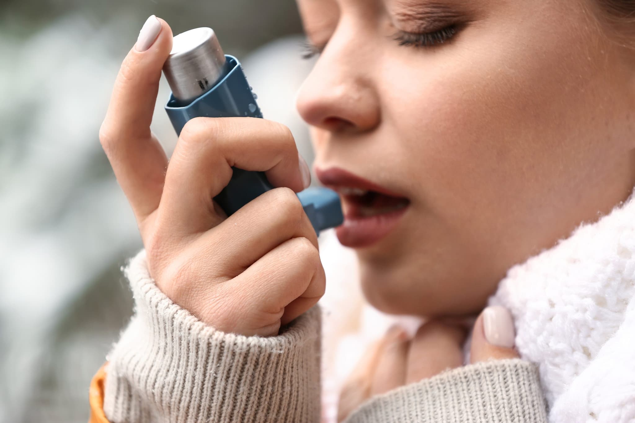 Young woman with inhaler having asthma attack outdoors, closeup