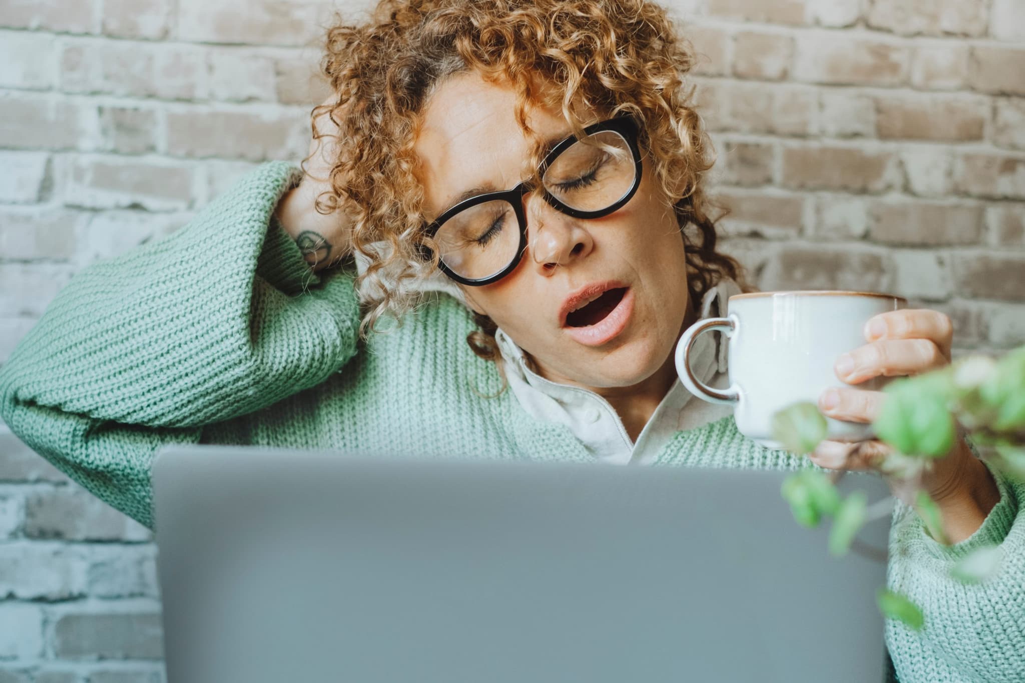 Picture of Tired woman suffering insomnia or narcolepsy working in front of. a laptop computer and drinking coffee for caffeine.