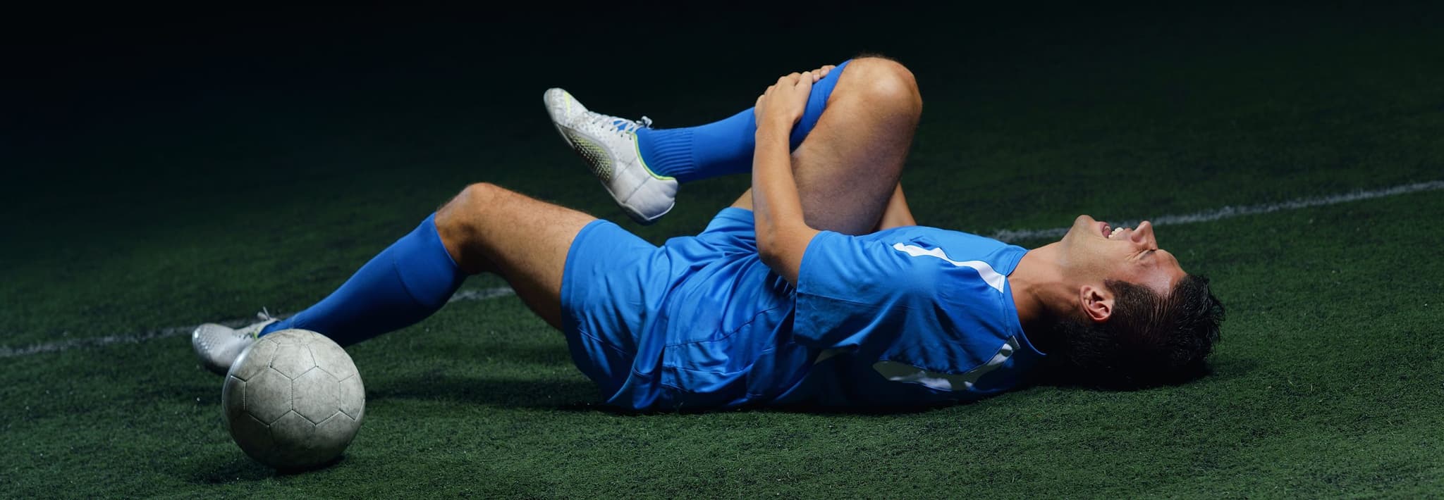 Picture of soccer player clutching knee on the floor in pain