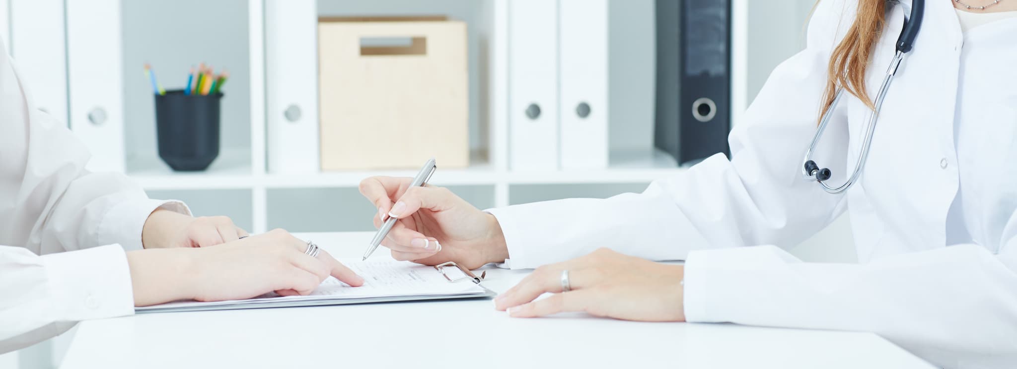 Young doctor explains how to fill out a medical form to female patient. Partnership, trust and medical ethics concept