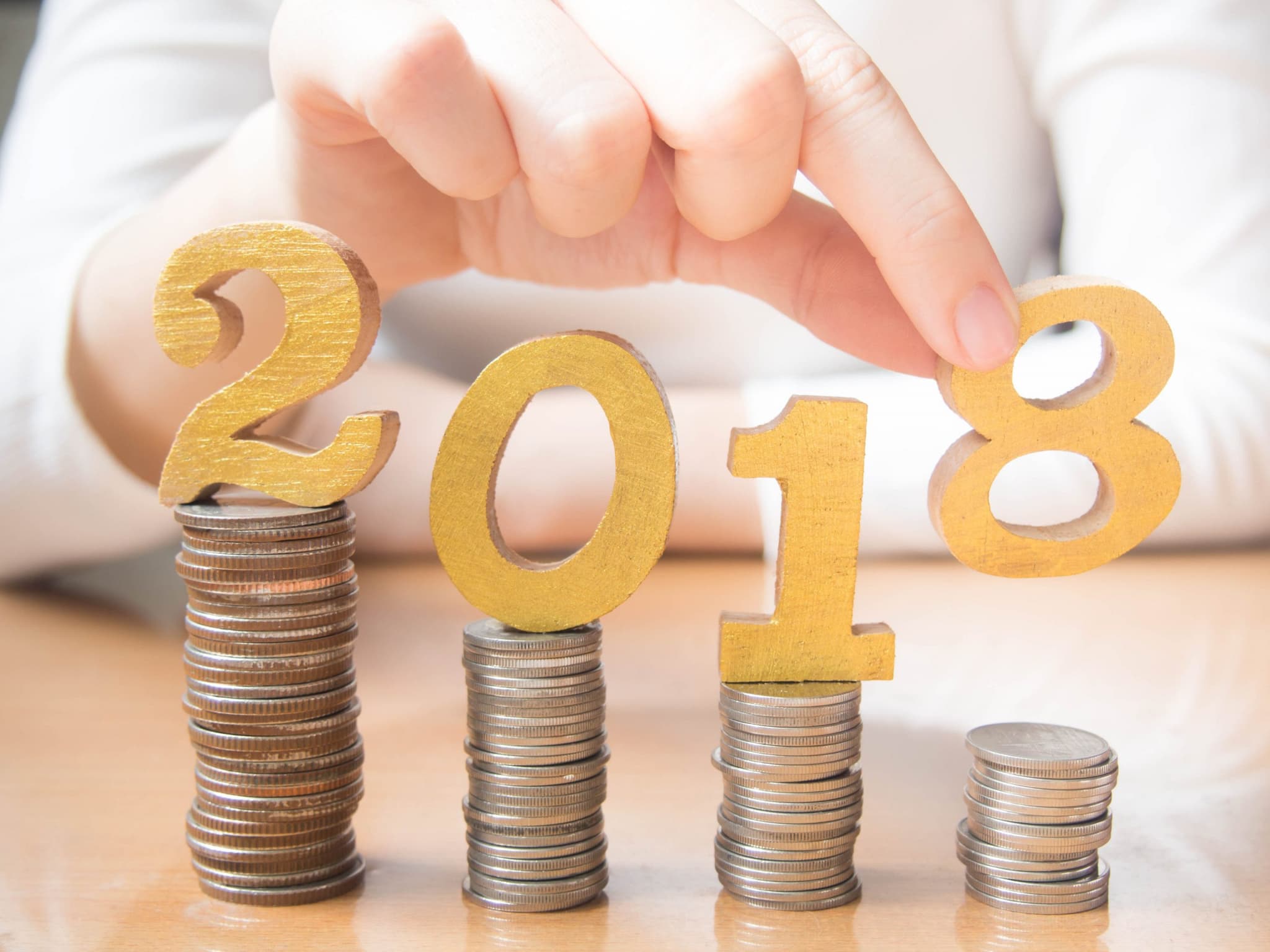2018 New year saving money and financial planning concept. Female hands putting gold wooden number 2018 on stack of coins. Creative idea for business growth, tax payment, investment and banking.