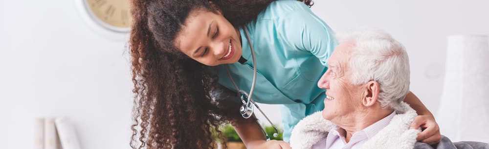 Picture of Panorama of a happy nurse with a stethoscope covering an elderly man with a blanket in a nursing home