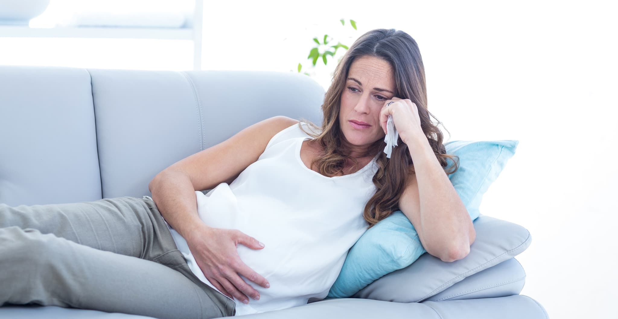 Sad pregnant woman lying on sofa