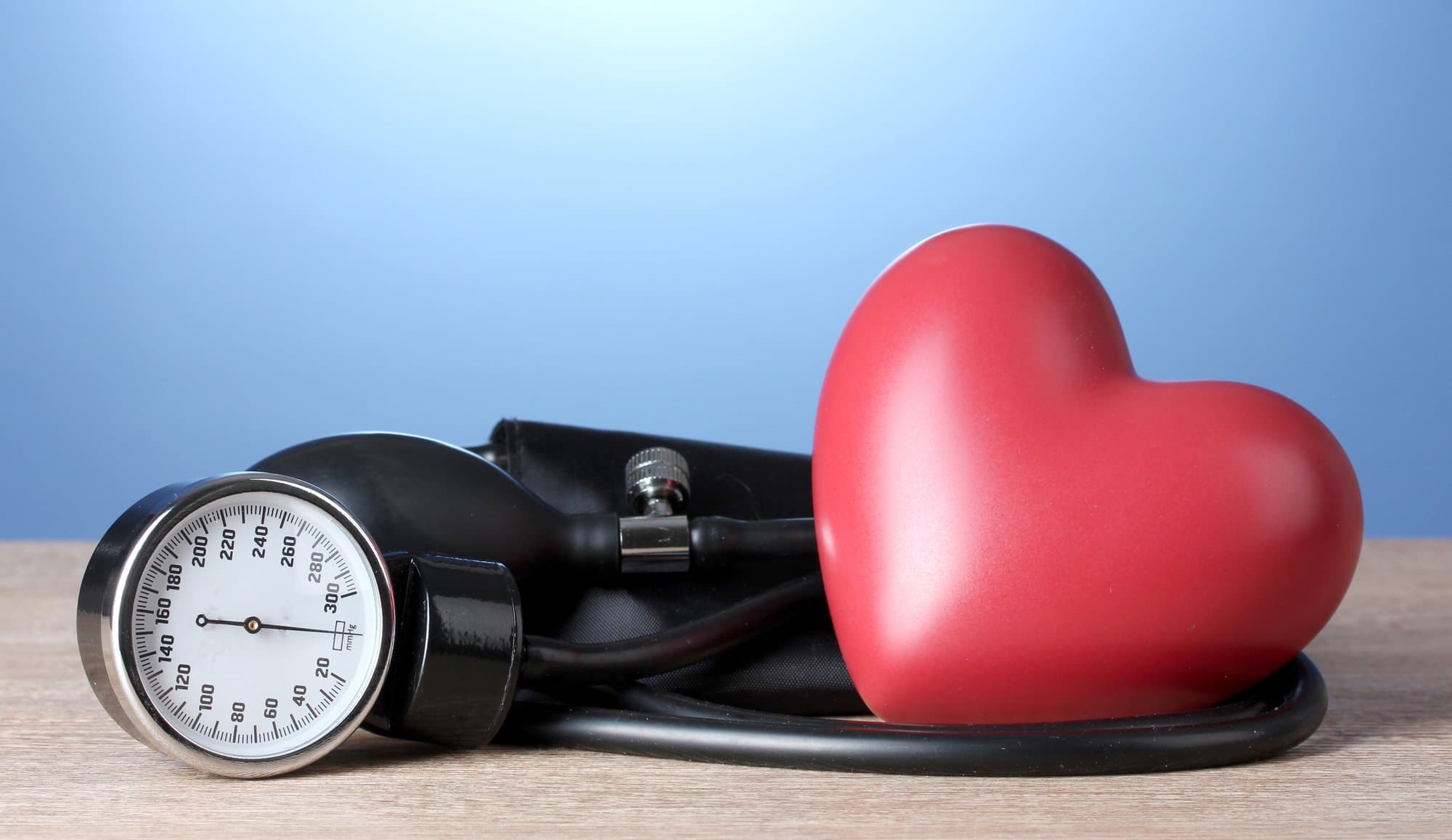 Black tonometer and heart on wooden table on blue background