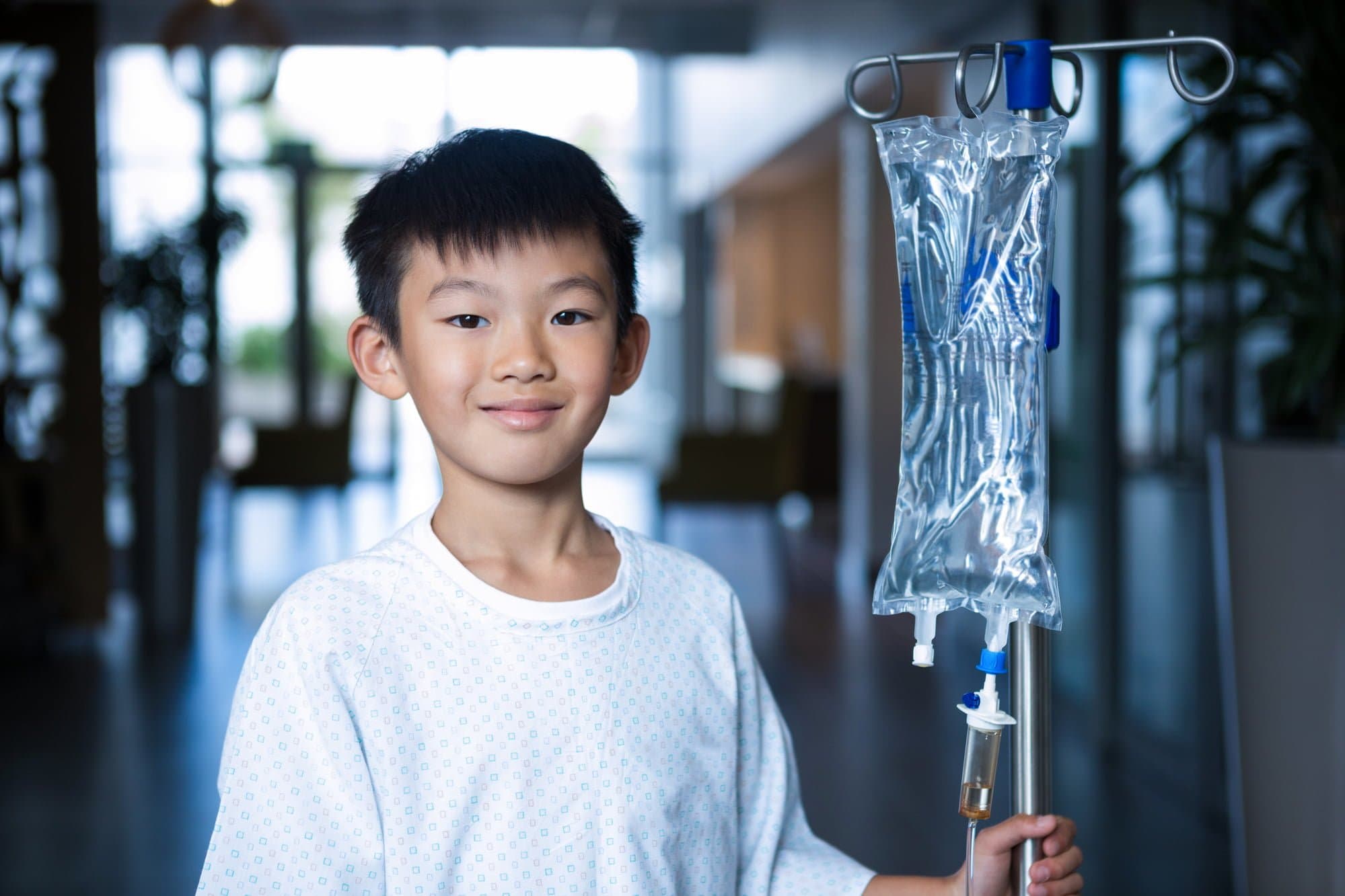 Picture of Smiling boy patient holding intravenous iv drip stand in corridor at hospital