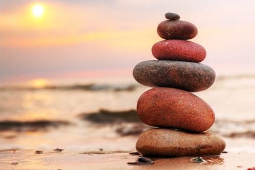 Picture of Stones pyramid on sand symbolizing zen, harmony, balance. Ocean at sunset in the background