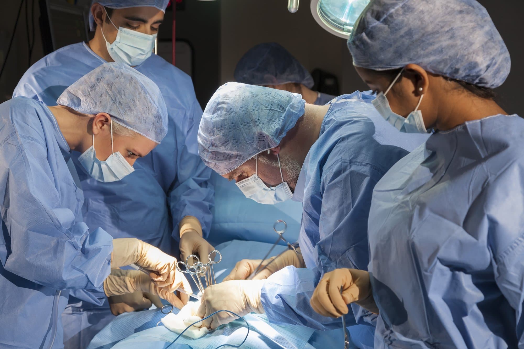 A team of interracial medical doctors male; female surgeons in surgery operating on a patient using different medical equipment instruments wearing scrubs and masks