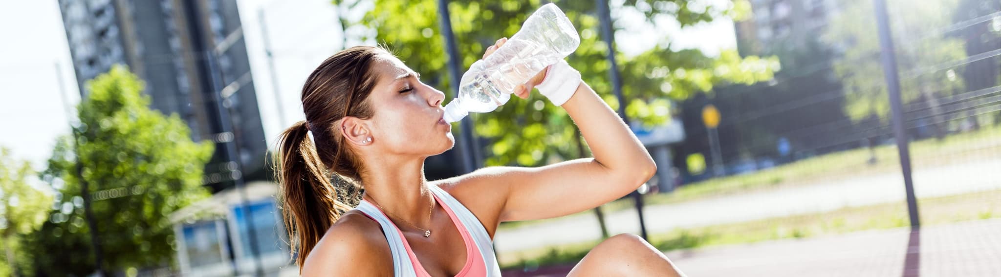 fit woman drinking water on yoga mat outside