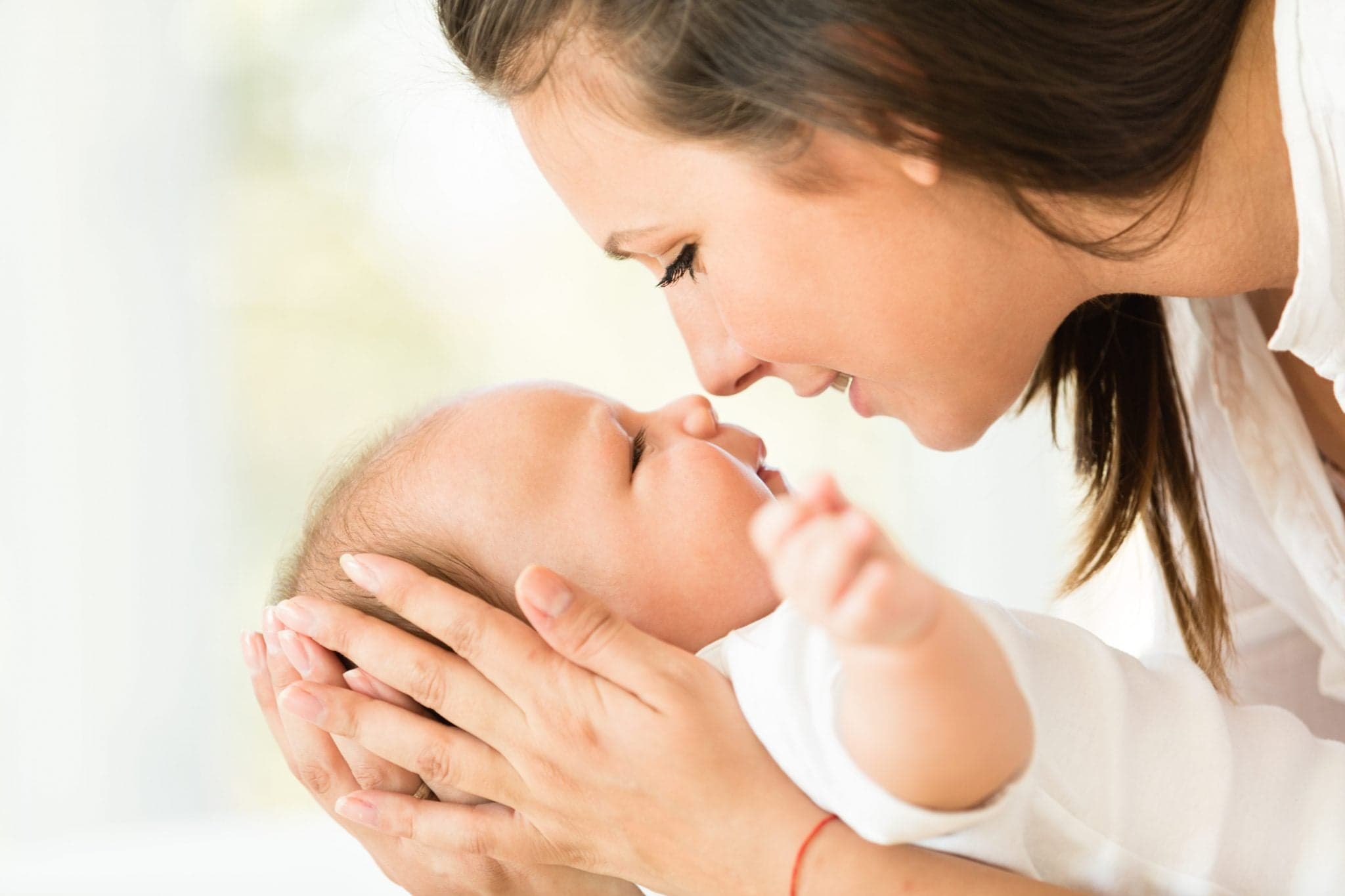 Picture of Side view and close-up of a happy young Caucasian mother playing with her cute three months old baby boy. They are face to face, baby is smiling and looking at his mother.