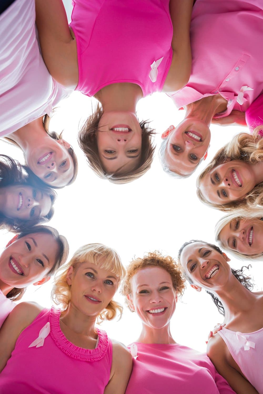 Group of women in circle wearing pink for breast cancer on white background