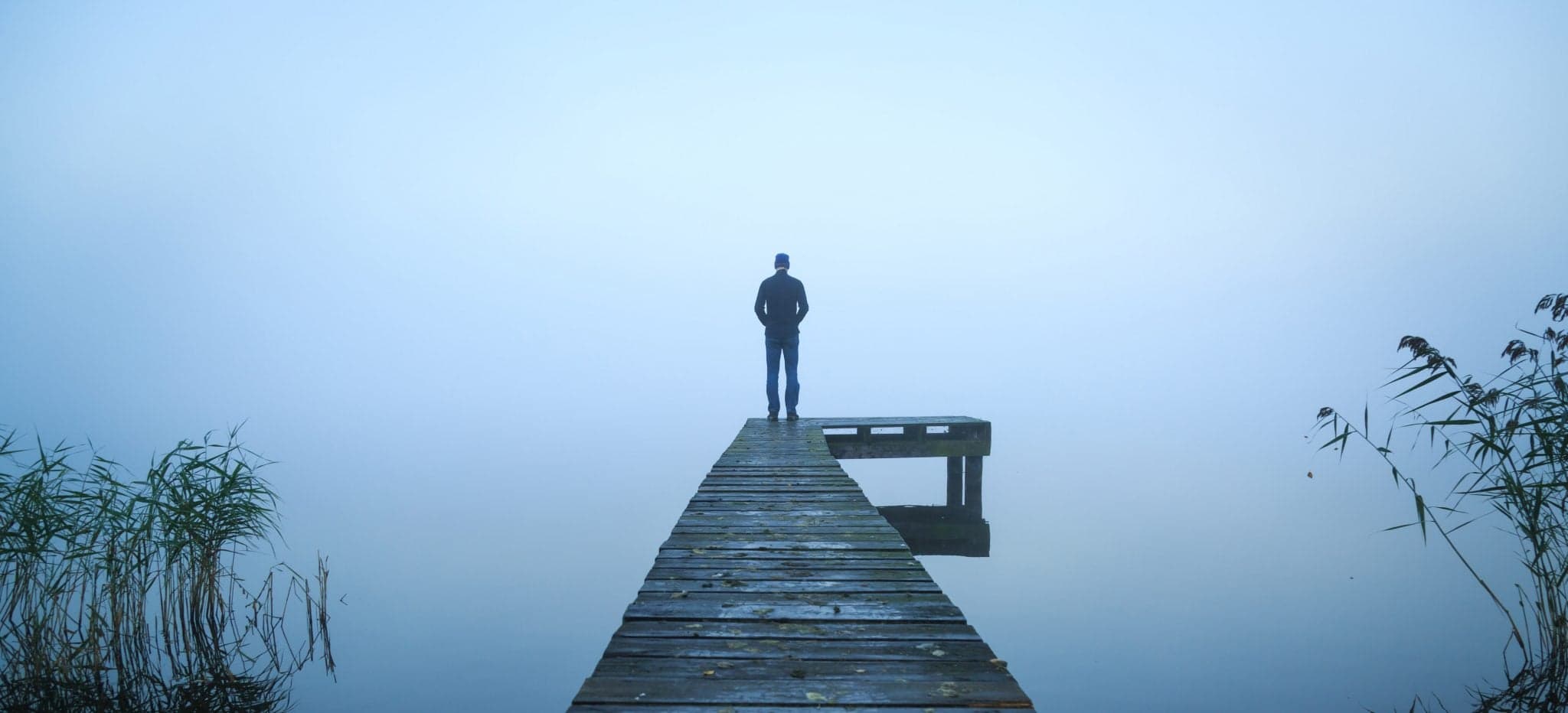 Depressed man standing alone on a jetty on a foggy autumn day.