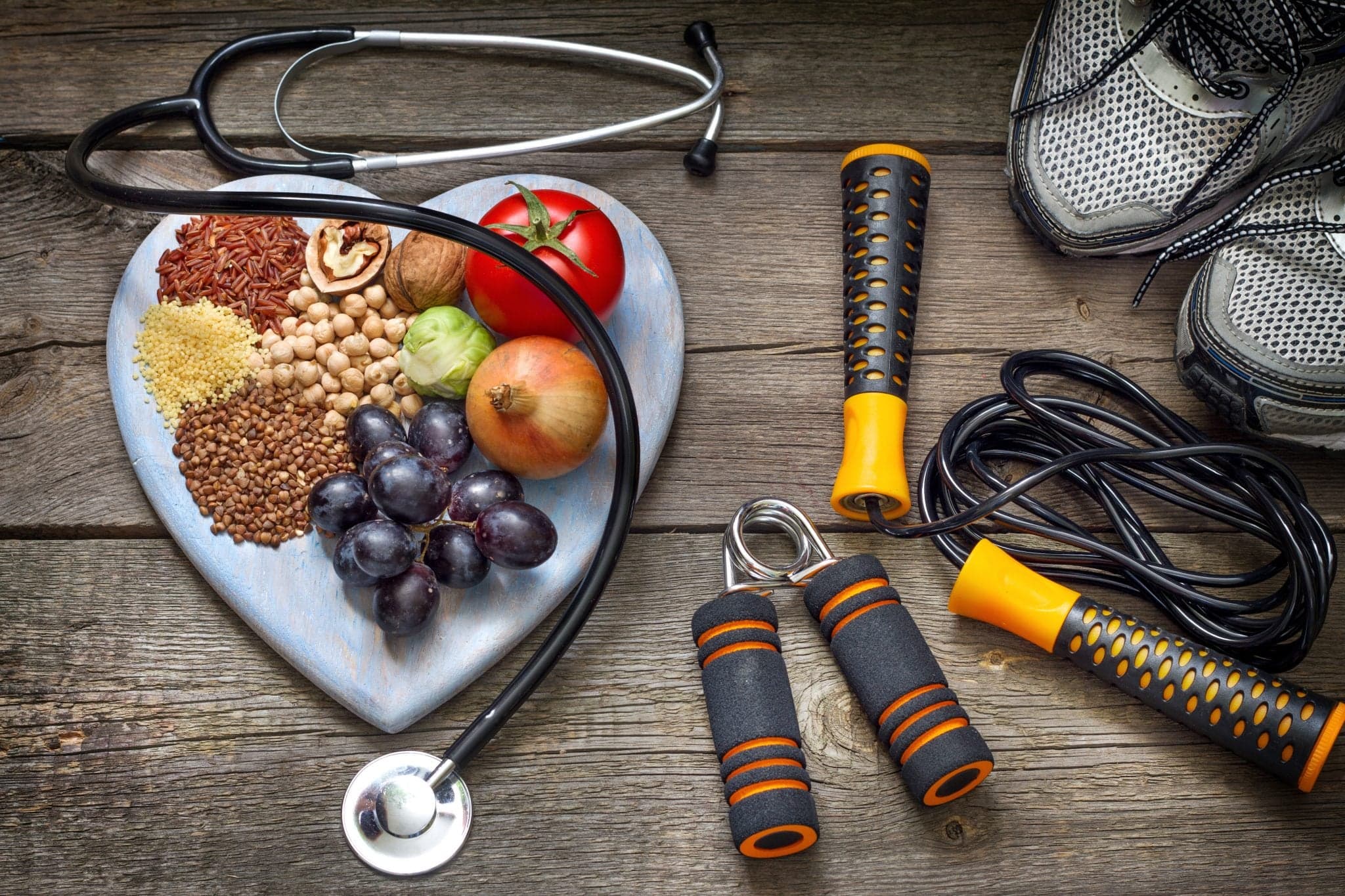 Healthy lifestyle concept with diet and fitness - heart plate with fruits and nuts on table next to workout equipment