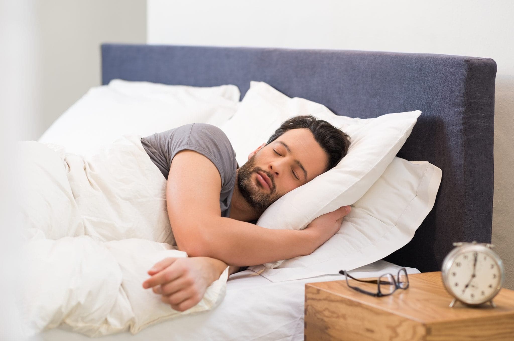 Picture of Handsome man sleeping in his bedroom. Man sleeping with alarm clock in foreground. Serene latin man sleeping peacefully.