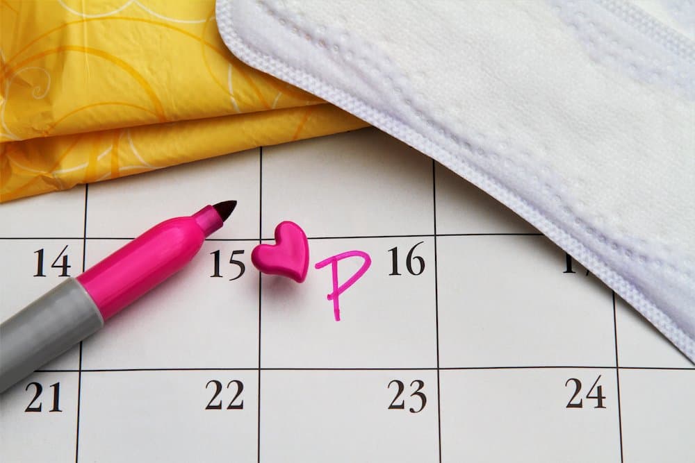 Picture of Calendar with date marked with heart push pin and letter P. Menstruation concept. Women's personal hygiene items: pads and liners.