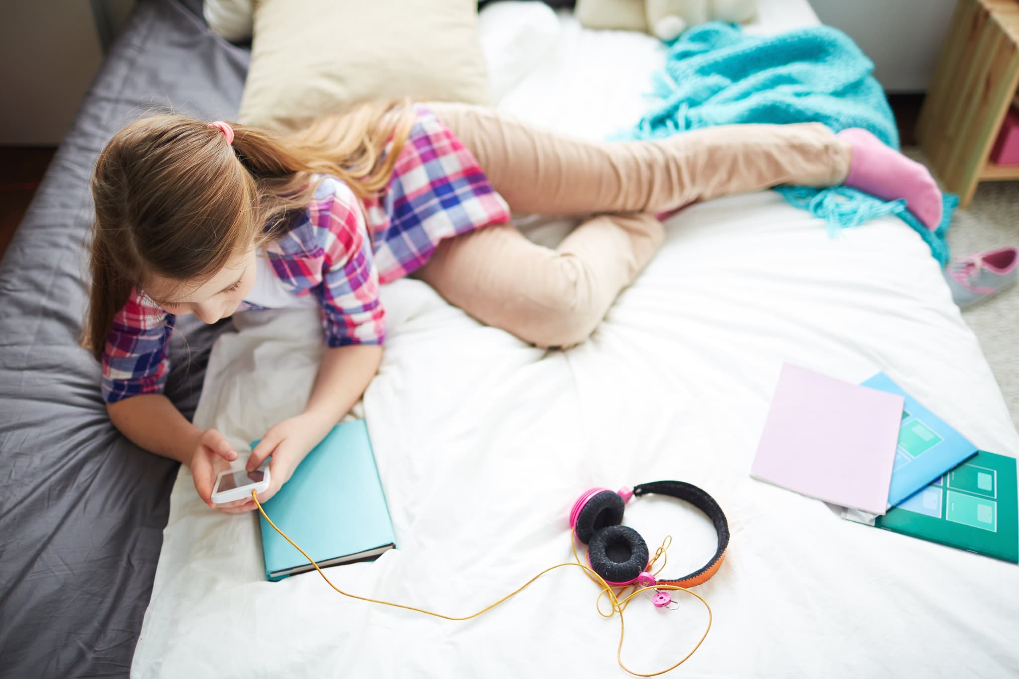 Pretty teenage girl with smartphone relaxing on bed