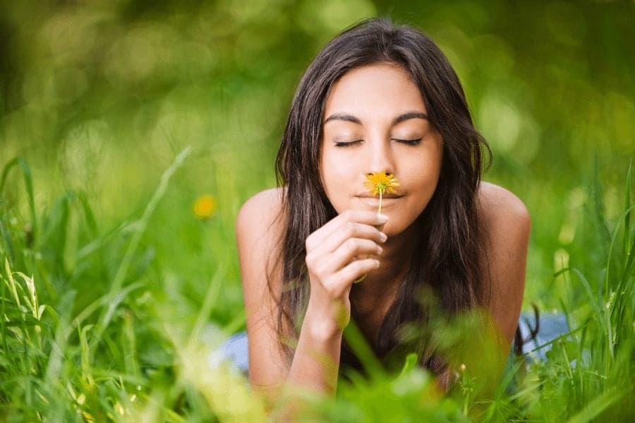 woman smelling flower in grassy field