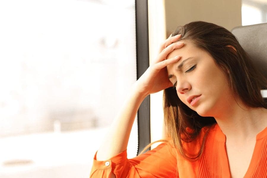 woman with headache on train leaning against window