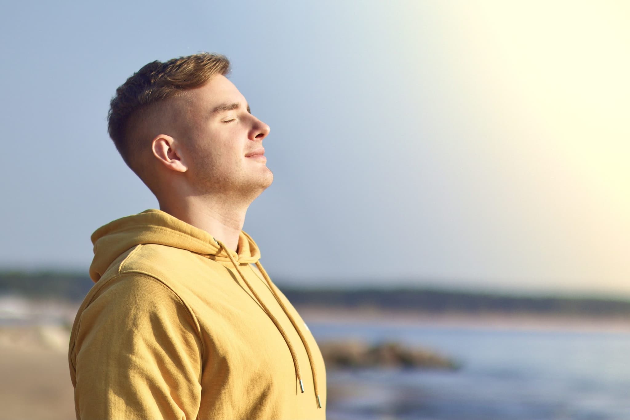Young man enjoying good weather on the beach, shore, breathing deep fresh sea air with eyes closed