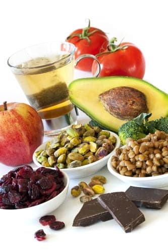 Foods rich in antioxidants, over white background. Includes cranberries, apple, green tea, tomatoes, broccoli, avocado, lentils, pistachios and dark chocolate.