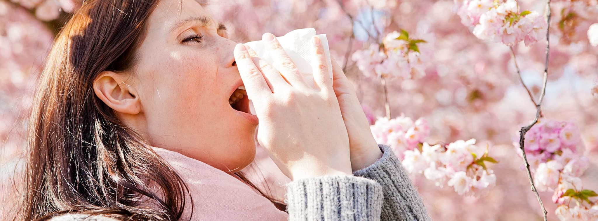 Picture of woman sneezing next to blossoming trees - Seasonal Allergies
