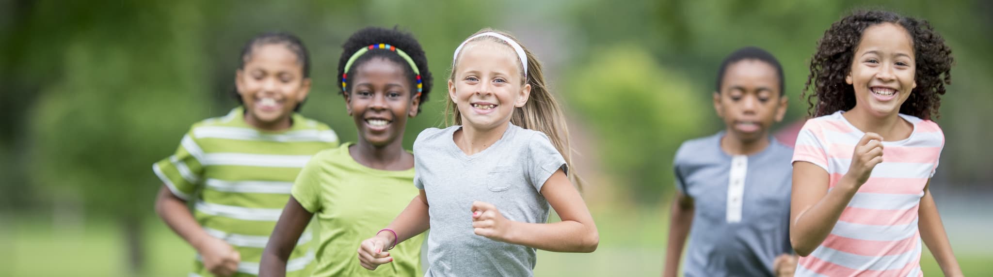 Picture of A multi-ethnic group of elementary age students are playing tag at the park during recess. They are happily chasing each other through the grass on a sunny day.
