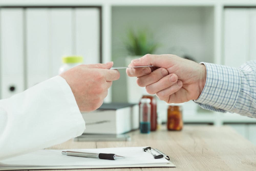 Picture of Doctor taking medical insurance card from patient in office during scheduled checkup