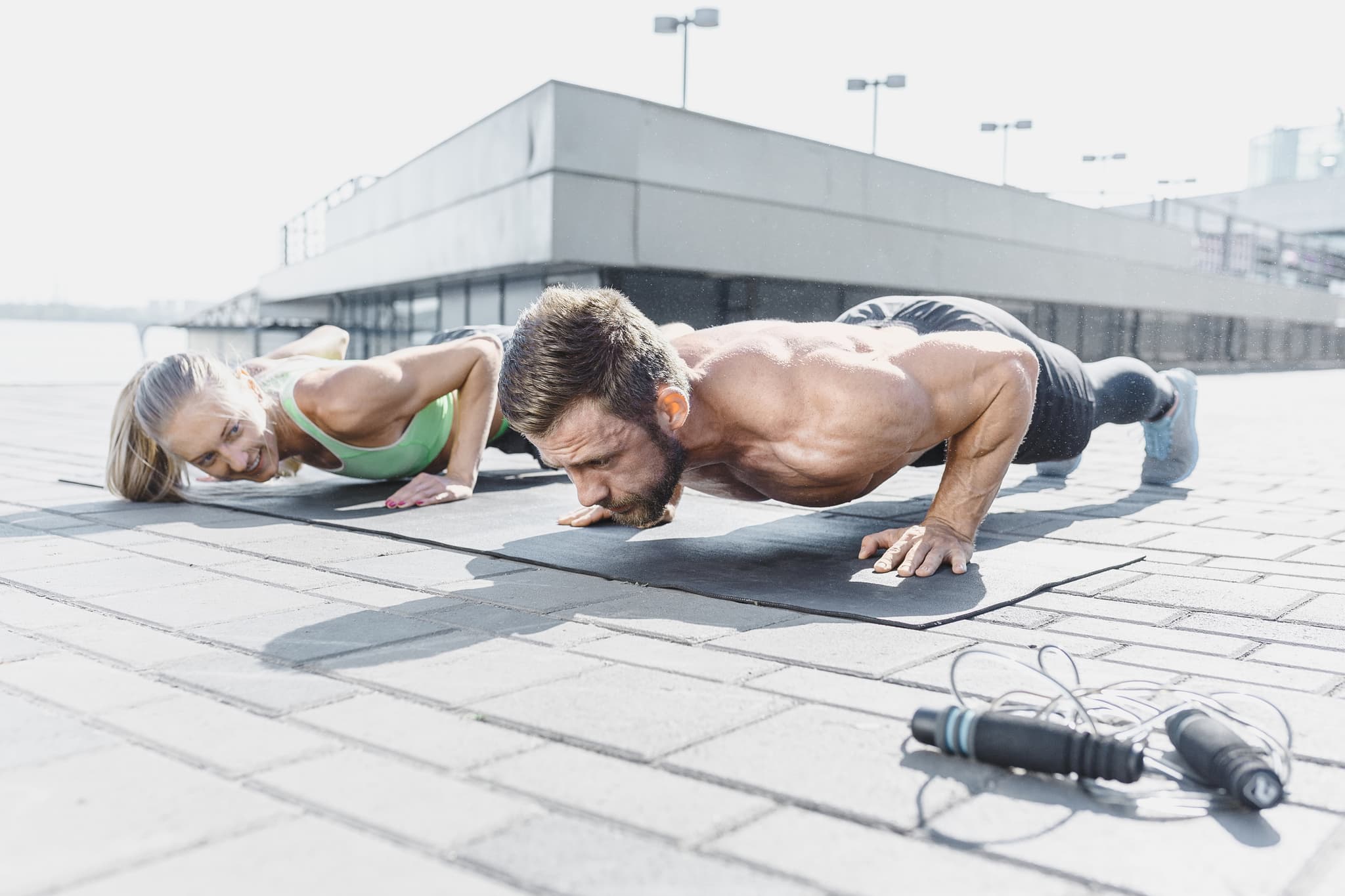 Fit fitness woman and man doing fitness exercises outdoors at city